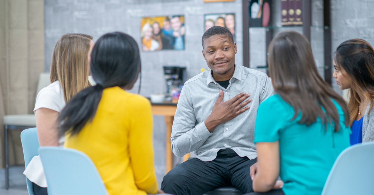 A childcare director sitting down with a group of educators, holding his palm to his heart and discussing empathy and acceptance in the center