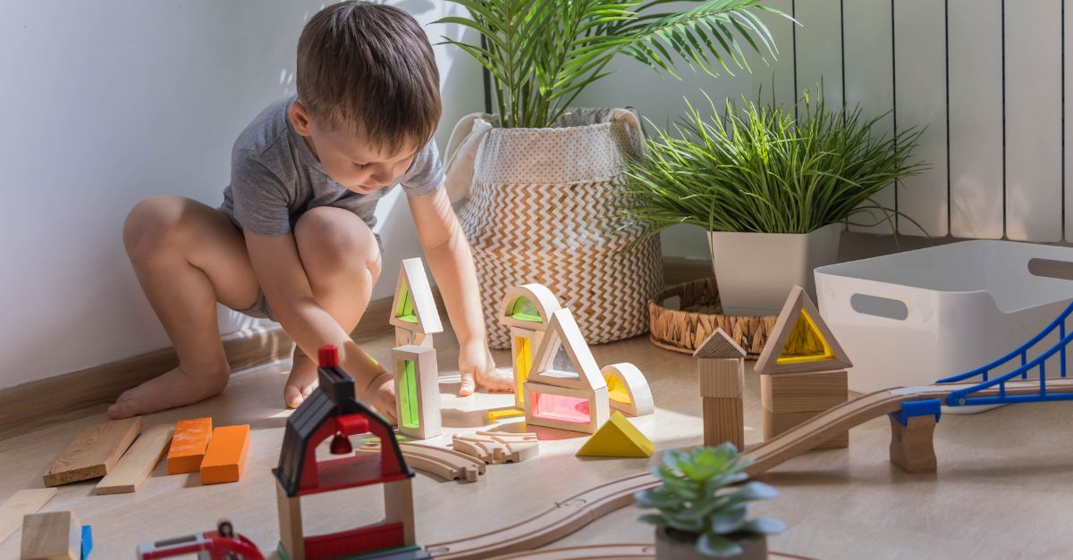 A preschool aged boy engaged in independent play as he builds a train track and stacks coloured blocks. 