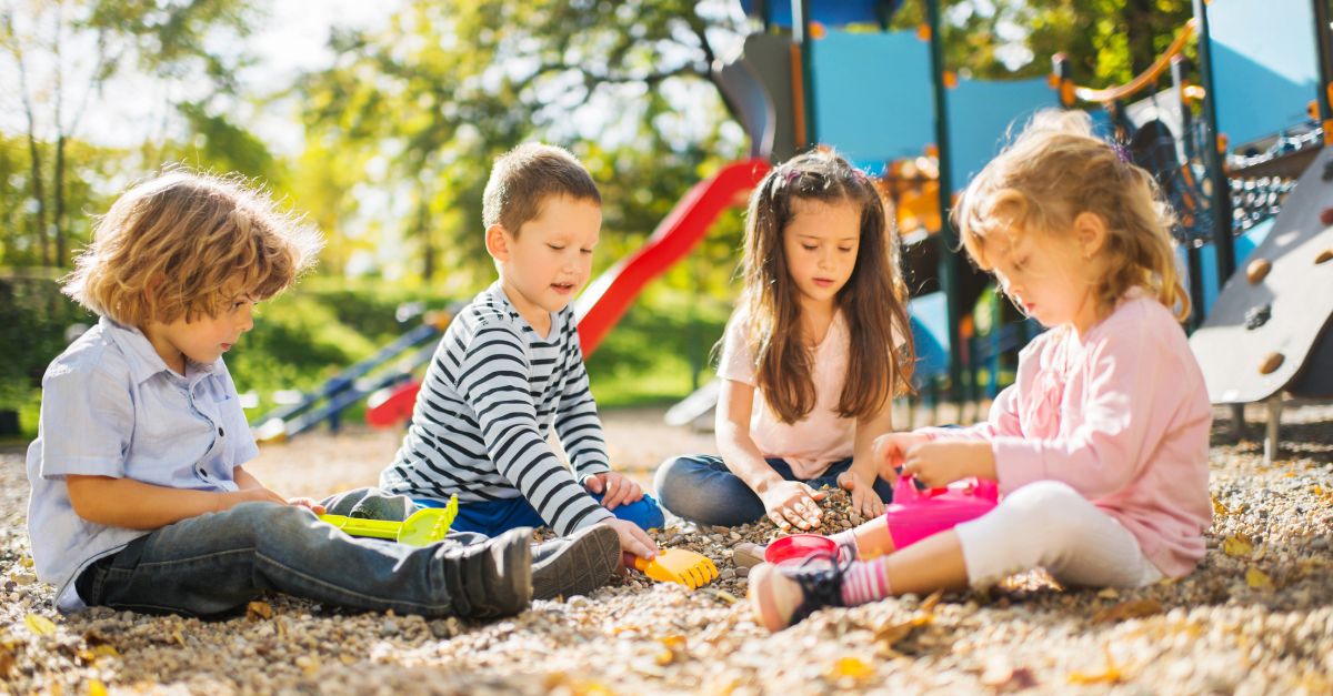 Four kindergarteners playing with sand and rocks on the outdoor playground