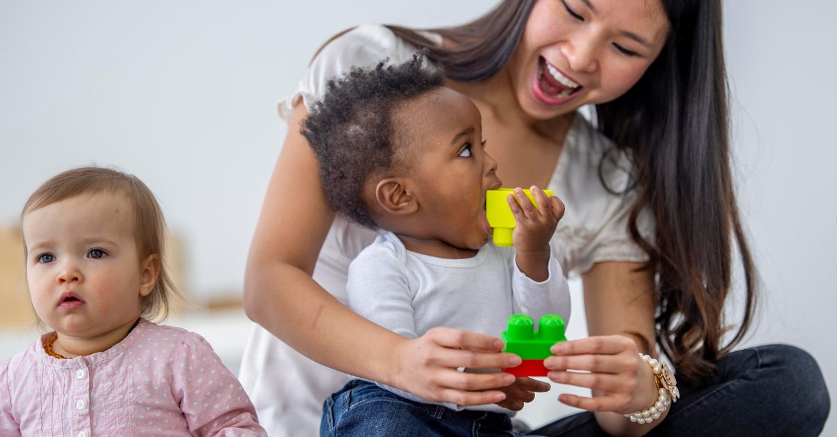 Early childhood educator playing with blocks with two infants in the classroom