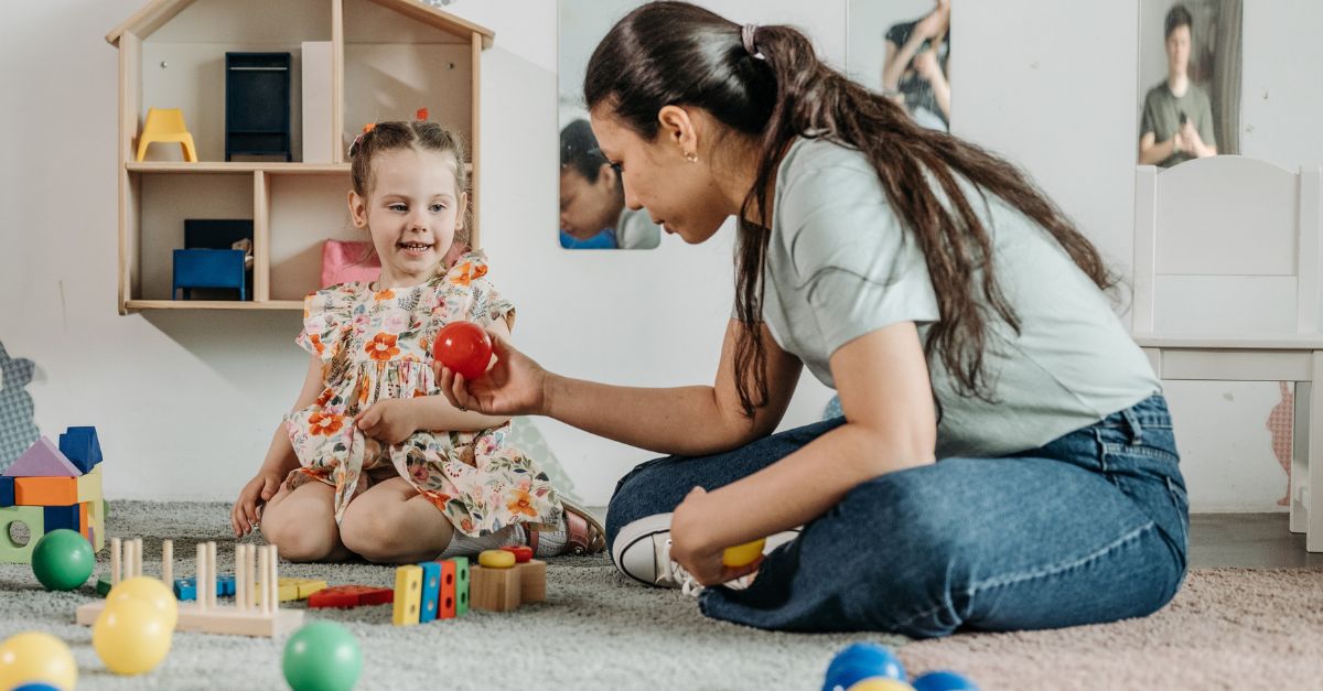 An early childhood educator playing with a preschool aged child on the floor in the classroom. Building with blocks and sharing materials. 