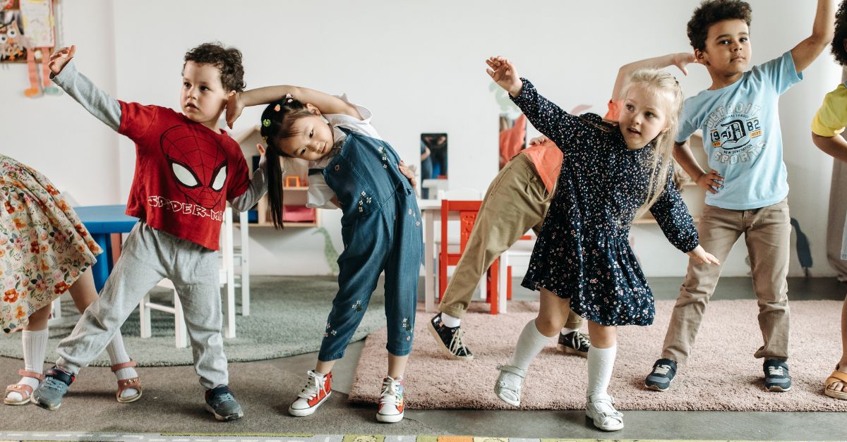 A group of kindergarten aged children practicing dancing and gross motor movements in the classroom. 