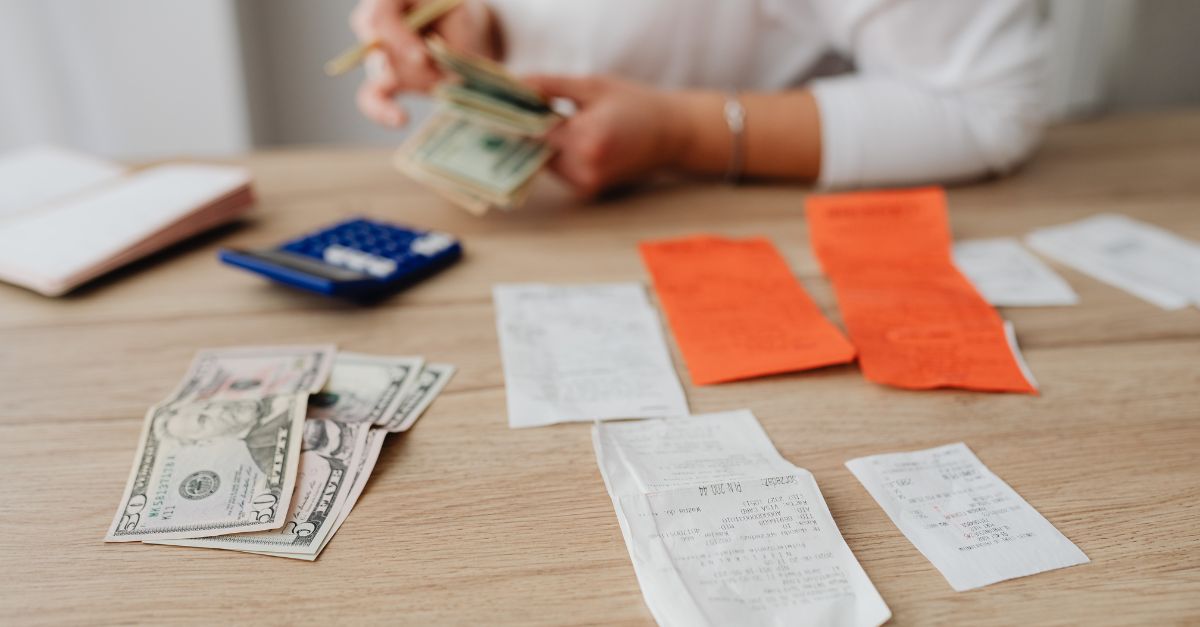 A wooden desk with cash, receipts and a calculator. A childcare director in the back tracking childcare payments. 