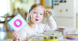 Preschooler holding up a card with the letter "O" as she practices saying "O" and building her letter recognition and phonemic awareness.