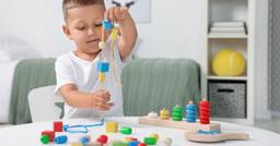 A preschool boy playing practicing fine motor skills as he threads large beads onto a rope