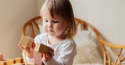 Female toddler playing independently with wooden blocks and exploring how to build towers.